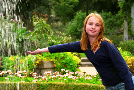 Young girl holding her hand under falling water in a gardenの写真素材