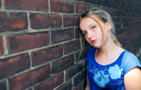 Young girl near brick wall looking upsetの写真素材