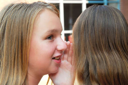 Two young teenage girls gossiping in school yard