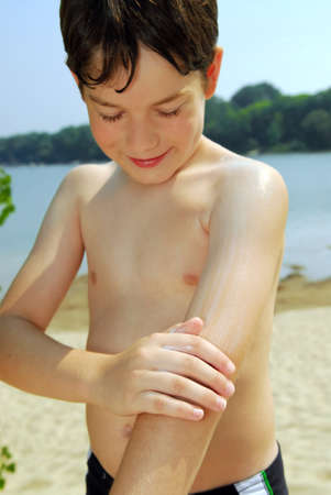 Young boy applying sunscreen to his skin on a beachの写真素材