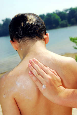 Children helping each other to apply sunscreen on a beachの写真素材