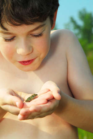 Young boy holding a tiny green frog in his handsの写真素材