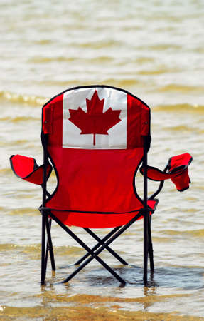 Folding chair with canadian flag design in shallow lake water, canadian vacation conceptの写真素材