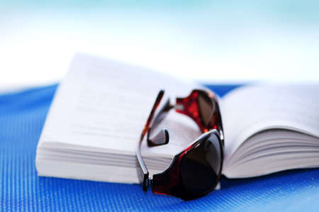 Sunglasses and open book on beach chair - summer vacation conceptの写真素材
