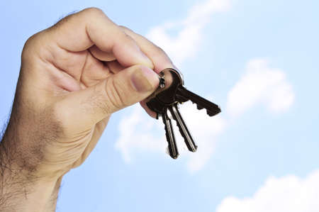 Man's hand holding house keys on blue sky backgroundの写真素材