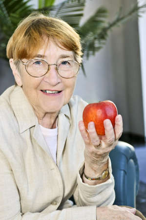 Elderly woman with glasses holding apple and smilingの写真素材