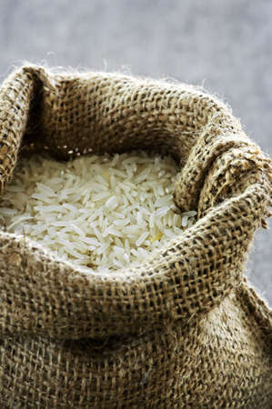 Raw long grain white rice grains in burlap bagの写真素材