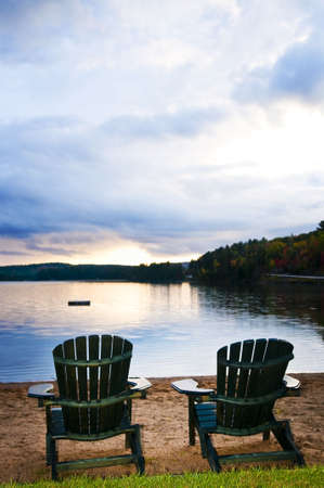 Two wooden chairs on beach of relaxing lake at sunsetの写真素材