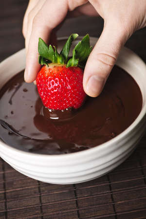 Hand dipping fresh strawberry in melted chocolateの写真素材