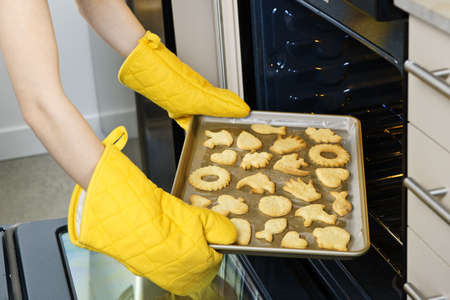 Taking fresh baked shortbread cookies from oven in kitchenの写真素材