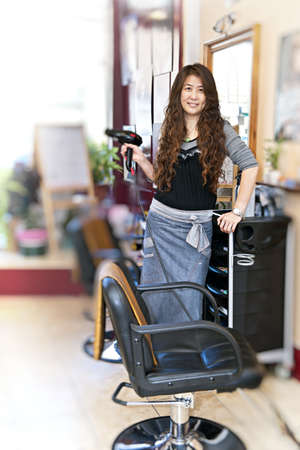 Happy hairdresser holding hairdryer in hair salonの写真素材