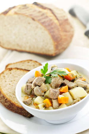 Bowl of hearty beef stew with vegetables served with rye breadの写真素材