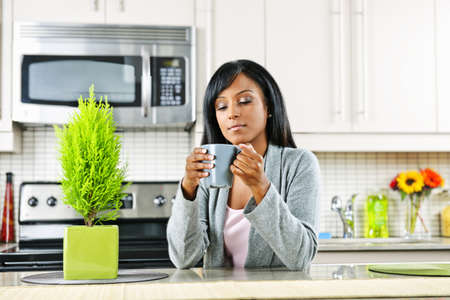 Thoughtful black woman holding coffee mug in modern kitchen interiorの写真素材