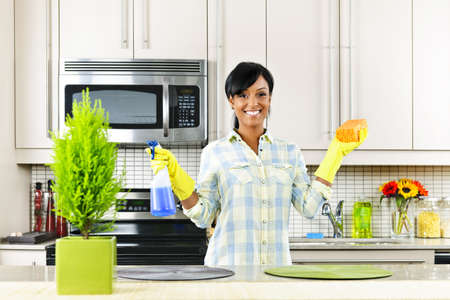Smiling young black woman with sponge and rubber gloves cleaning kitchenの写真素材