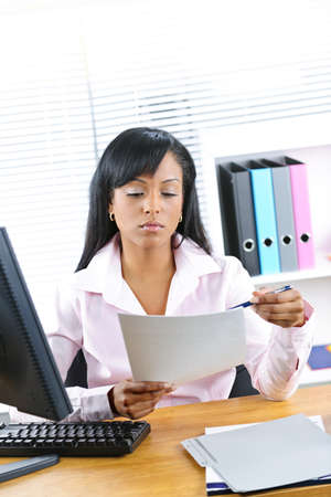 Young black business woman reading document at desk in officeの写真素材