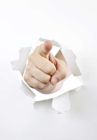 Finger pointing through hole torn in white paperの写真素材