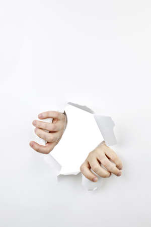 Hands ripping a hole in white paper with torn edges