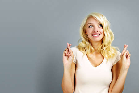 Smiling blonde caucasian woman with fingers crossed on gray backgroundの写真素材