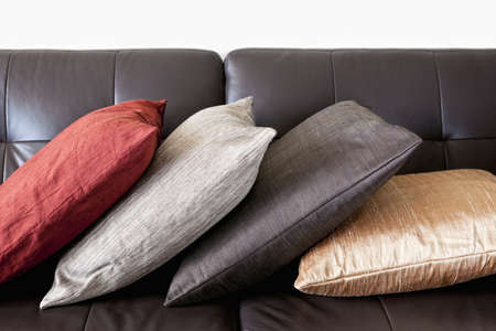 Four colorful cushions on dark brown leather couchの写真素材