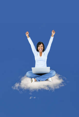 Happy black woman with computer sitting on cloudの写真素材
