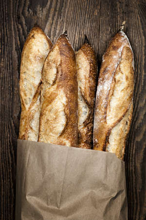 Four baguette bread loaves in paper bag on wooden backgroundの写真素材