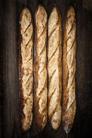 Four whole baguette bread loaves on dark wooden backgroundの写真素材