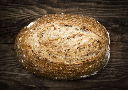 Artisan loaf of freshly baked multigrain bread on wooden background
