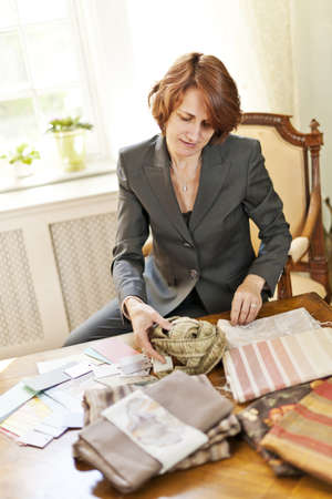 Female interior designer choosing from fabric samples sitting at deskの写真素材