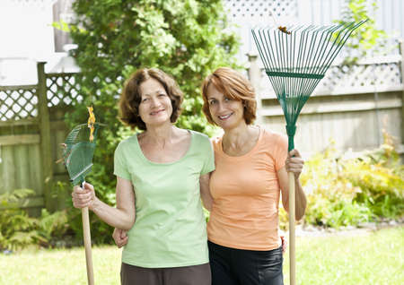 Mother and daughter holding rakes gardening doing yard work outsideの写真素材