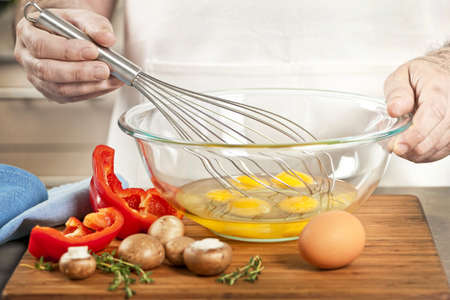 Closeup on man's hands whisking eggs in bowl for cooking omelet with vegetablesの写真素材