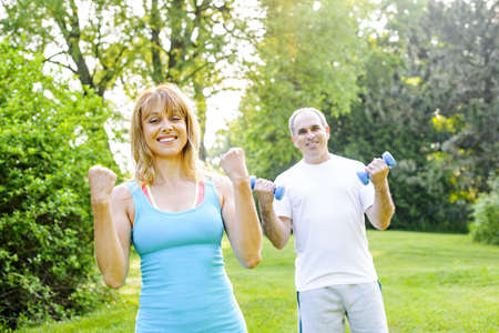 Female fitness instructor exercising with middle aged man in green parkの写真素材
