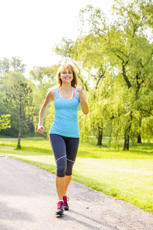 Smiling woman exercising on running path in green summer park Smiling woman exercising on running path in green summer park