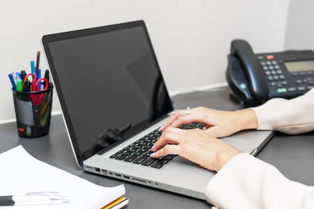 Female hands typing on laptop keyboard at office deskの写真素材