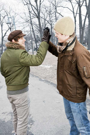 Two young men meeting in winter park giving high fiveの写真素材