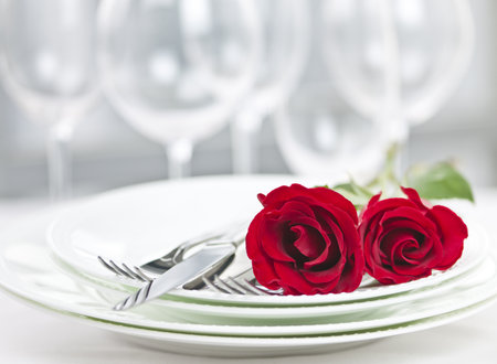Romantic restaurant table setting for two with roses plates and cutleryの写真素材