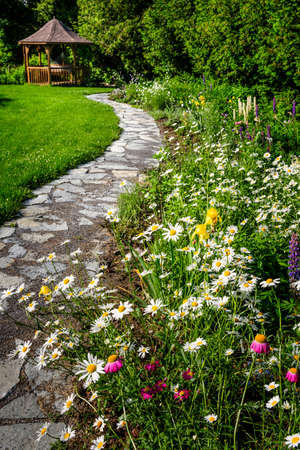 Wildflower garden with paved path leading to gazebo and blooming daisiesの写真素材