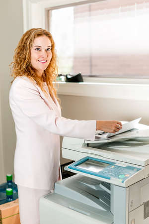 Smiling business woman operating photocopy machine in officeの写真素材