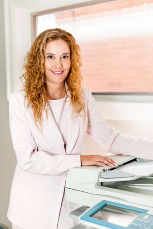 Smiling business woman operating photocopy machine in officeの写真素材