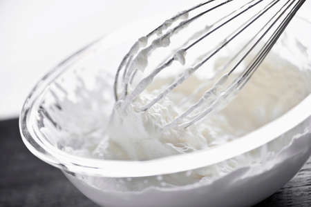 Closeup of metal whisk whipping cream in glass bowl