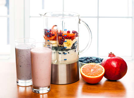 Prepared smoothies and healthy smoothie ingredients in blender with fresh fruit ready to blend on kitchen tableの写真素材
