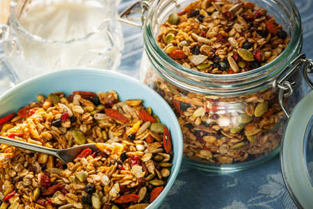 Serving of homemade granola in blue bowl and milk or yogurt on table with linensの写真素材