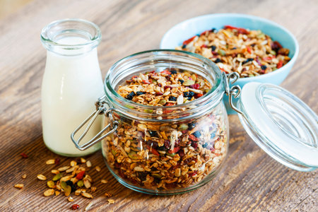 Homemade granola in open glass jar and milk or yogurt  on rustic wooden backgroundの写真素材