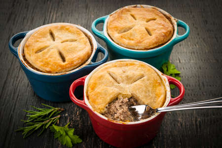 Three homemade gourmet meat pies with fork in ground beef filling on rustic wood background