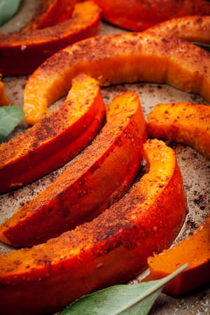 Sliced and spiced raw pumpkin pieces on roasting tray prepared for cookingの写真素材