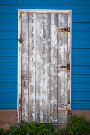 Old weathered wooden door on side of blue building. Prince Edward Island, Canada.の写真素材