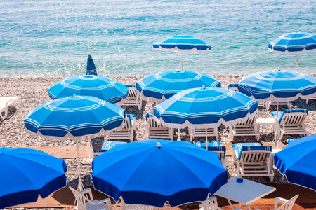 Blue umbrellas and chairs on pebble beach in Nice, France.の写真素材