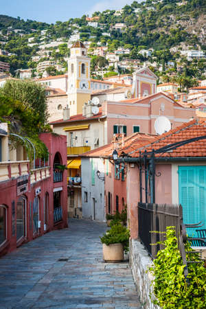 VILLEFRANCHE-SUR-MER, FRANCE - OCTOBER 4, 2014: Cobblestone street with colourful buildings leads to the heart of old town and Eglise Saint-Michel (Saint Michael's Church).のeditorial素材