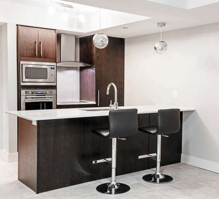 Modern luxury kitchen interior with dark wood cabinets, island counter, bar stools and stainless steel appliancesの写真素材