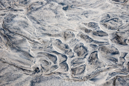Grey and beige abstract background of wet sand texture formed by flowing water on beach