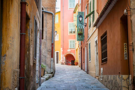 Narrow cobblestone street with bright buildings in medieval town Villefranche-sur-Mer on French Riviera, France.の写真素材